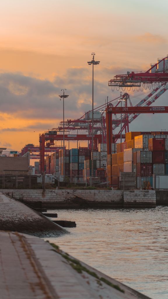 Colorful shipping containers and cranes at a port during sunset.